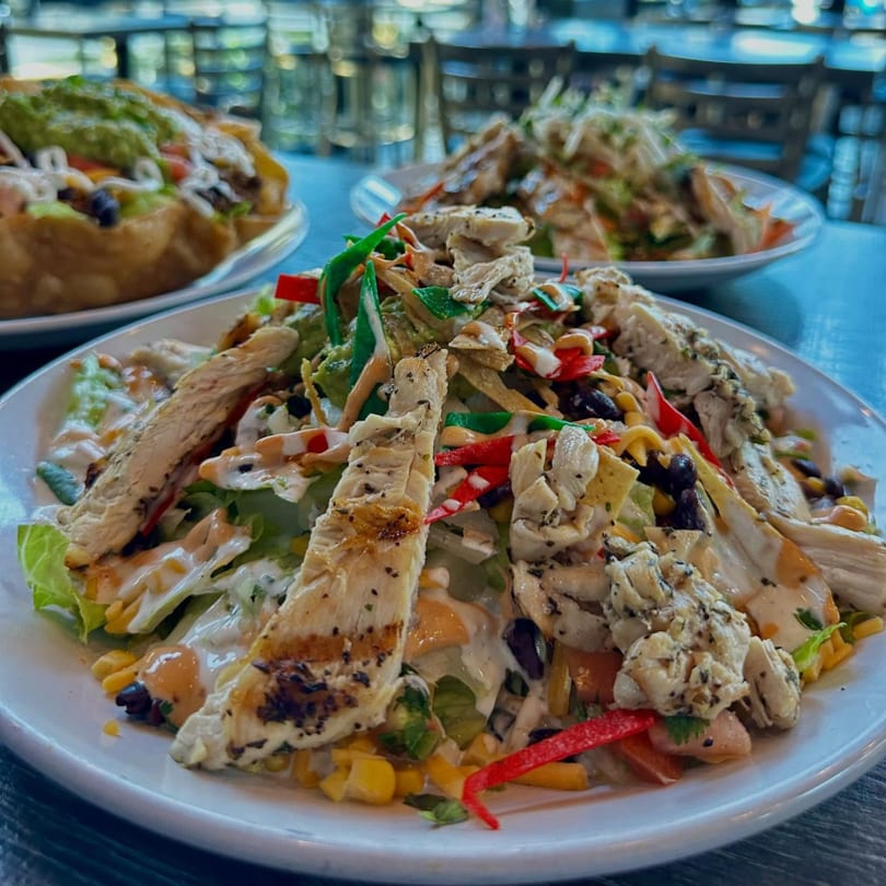 Close-up of a chicken salad with corn, black beans, tortilla strips, and dressing.